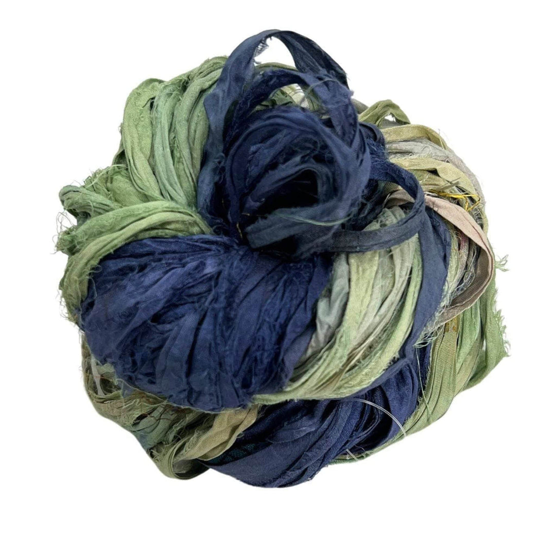 A ball of blue and green fabric strips rolled together on a white background.