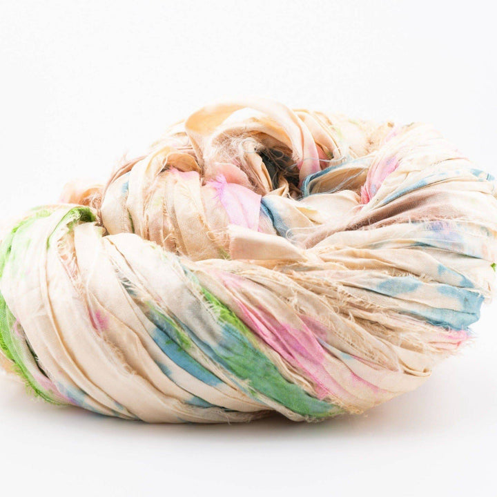 Loosely coiled off-white fabric with pastel tie-dye patterns in greens, pinks, and blues.